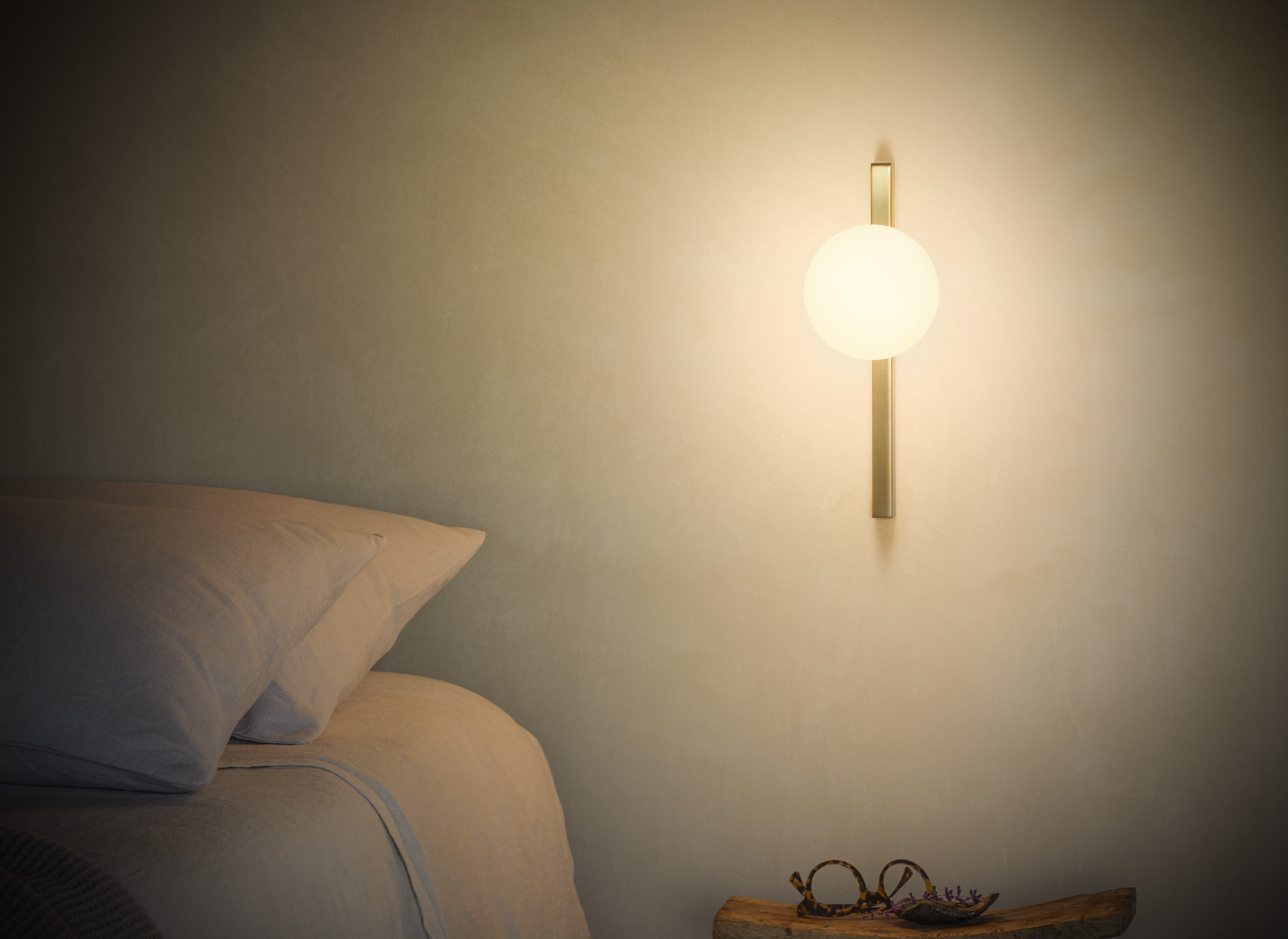 Ideal Lux opal globe wall light with a vertical brass-coloured frame beside a bed