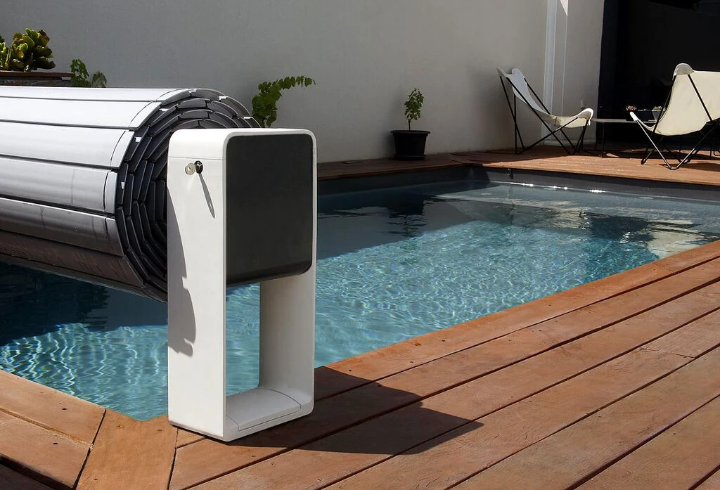 AstralPool Octeo automatic cover roller beside a pool with its grey slatted cover rolled up